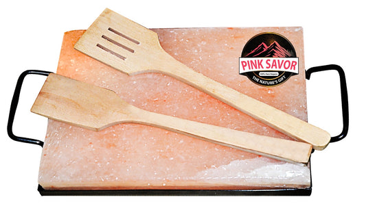 Cooking slab made of pink salt with wooden spatula and grill stand for healthy meal preparation.